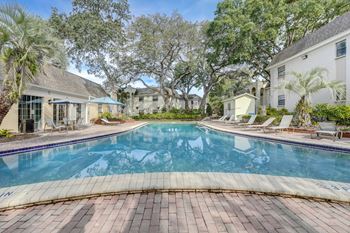 A swimming pool surrounded by a brick patio and palm trees.